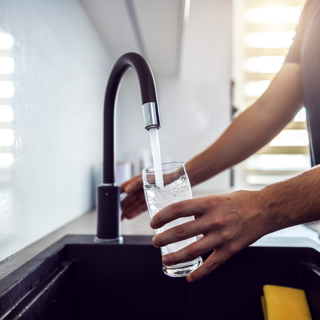 Close up of young man pouring fresh water from kitchen sink. Home interior.